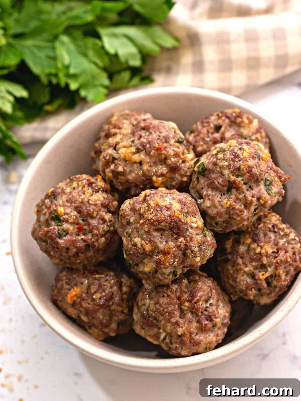 A bowl of perfectly golden-brown, Italian seasoned baked meatballs, garnished with fresh parsley.