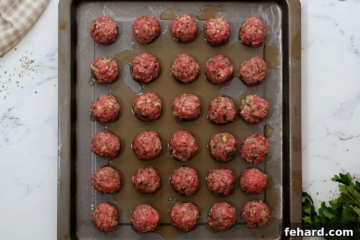 Shaped meatballs arranged on a baking sheet with a small amount of beef broth poured around them.