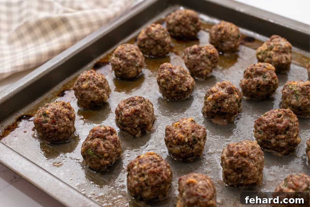 A rimmed sheet pan filled with perfectly baked, golden-brown meatballs.