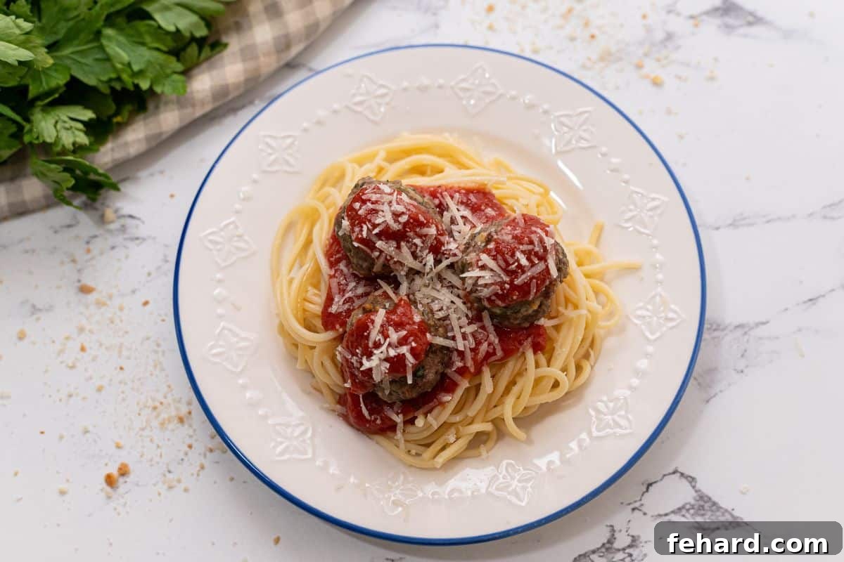 Baked meatballs served on a white plate with pasta, spaghetti sauce, and a generous sprinkle of parmesan cheese.