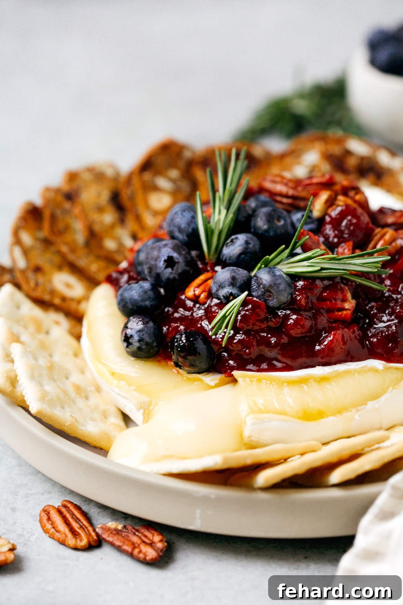 Close up of a baked brie with cranberry sauce cut open with cheese melting out, showing its gooey texture.