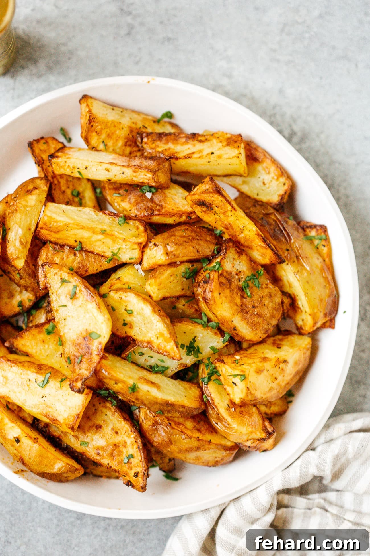A plate filled with golden brown, crispy air fryer potato wedges, garnished with fresh parsley.