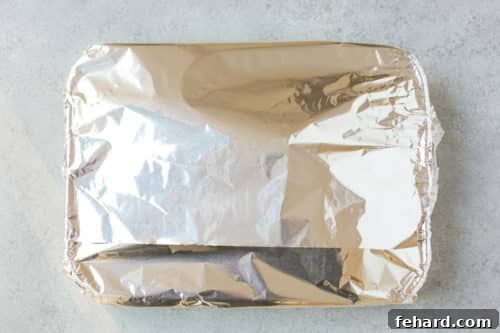 Leg of lamb in a roasting pan, tightly wrapped with aluminum foil.