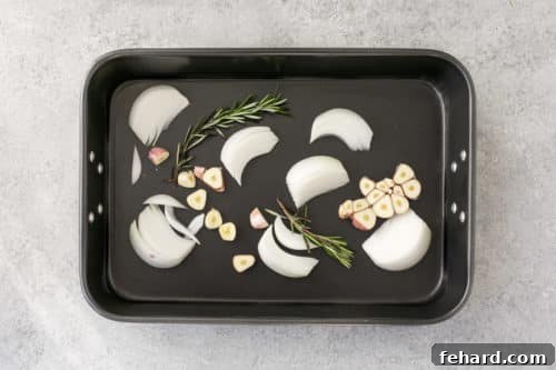 Chopped onions, garlic, and rosemary forming a bed in a roasting pan.