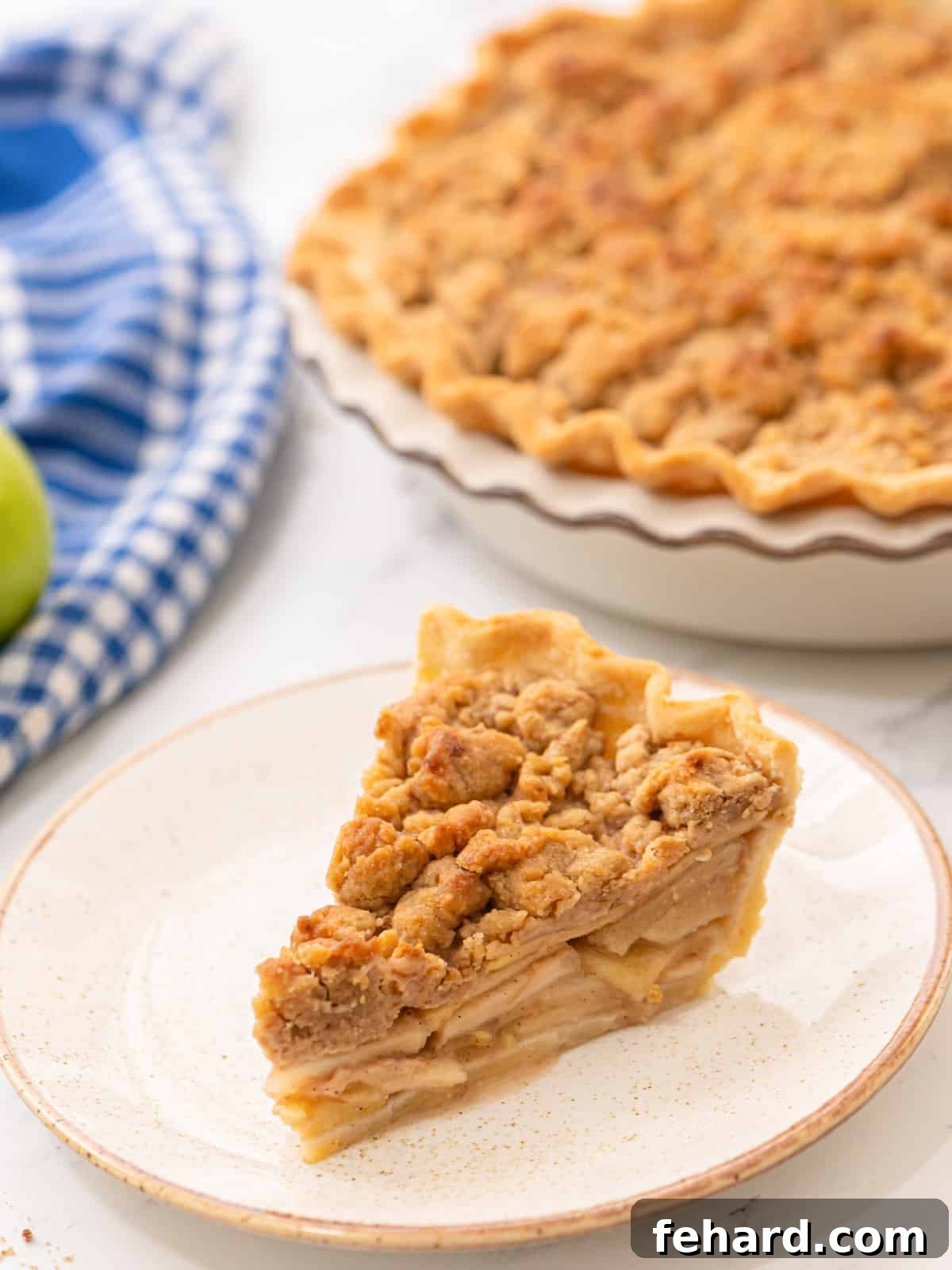 Delicious Slice of Dutch Apple Pie A beautifully baked slice of Dutch Apple Pie on a white plate, showcasing its golden brown streusel topping, tender apple filling, and flaky crust. The rest of the pie is visible in the background.