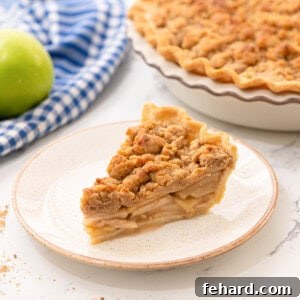 Buttery Streusel Apple Pie 2 A perfectly baked slice of Dutch Apple Pie on a white plate, with the full pie blurred in the background, showcasing its golden streusel topping and flaky crust.