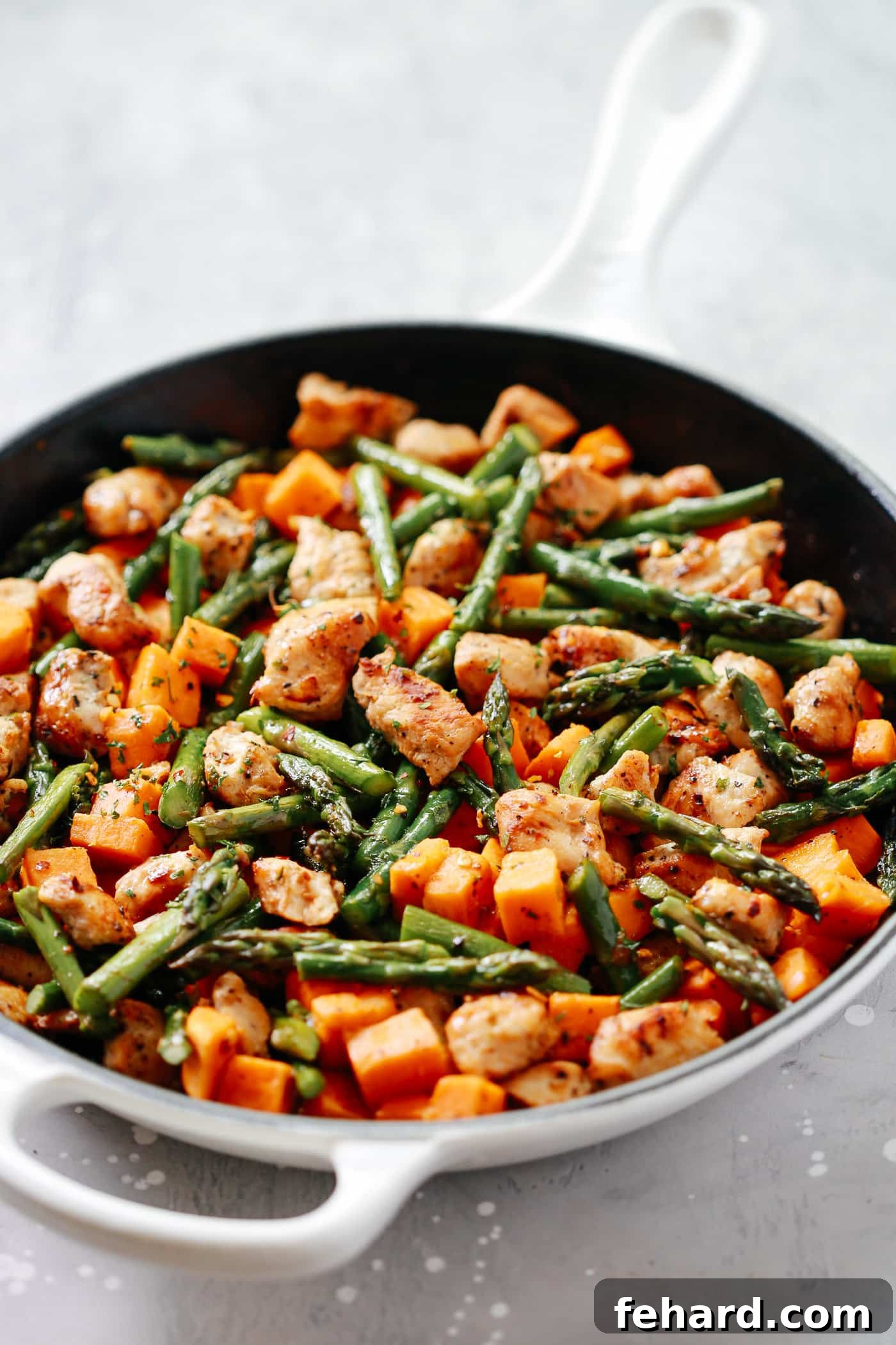 A tantalizing closeup of a perfectly cooked one-pan chicken sweet potato and asparagus skillet, glistening with savory juices and ready to be served.
