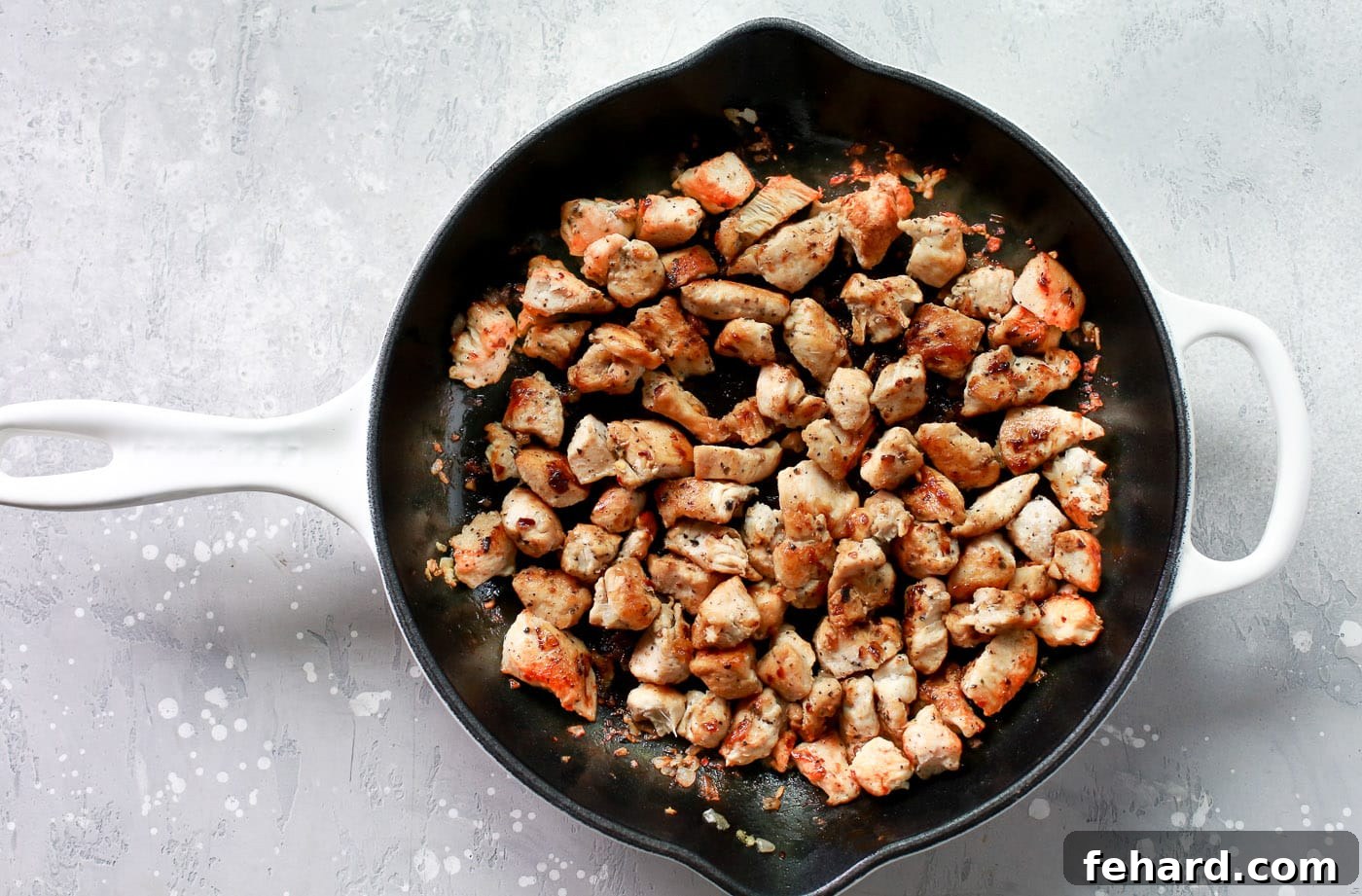 Bite-sized pieces of chicken cooking in a hot skillet with garlic, acquiring a golden-brown sear.
