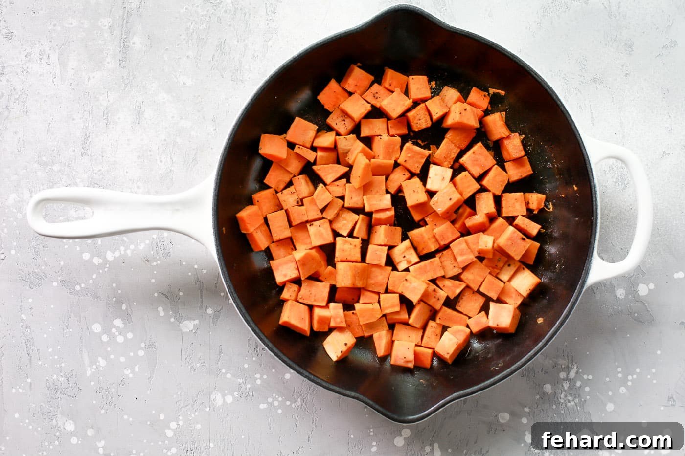 Uniformly diced sweet potatoes simmering gently in chicken broth within the skillet, covered to steam.