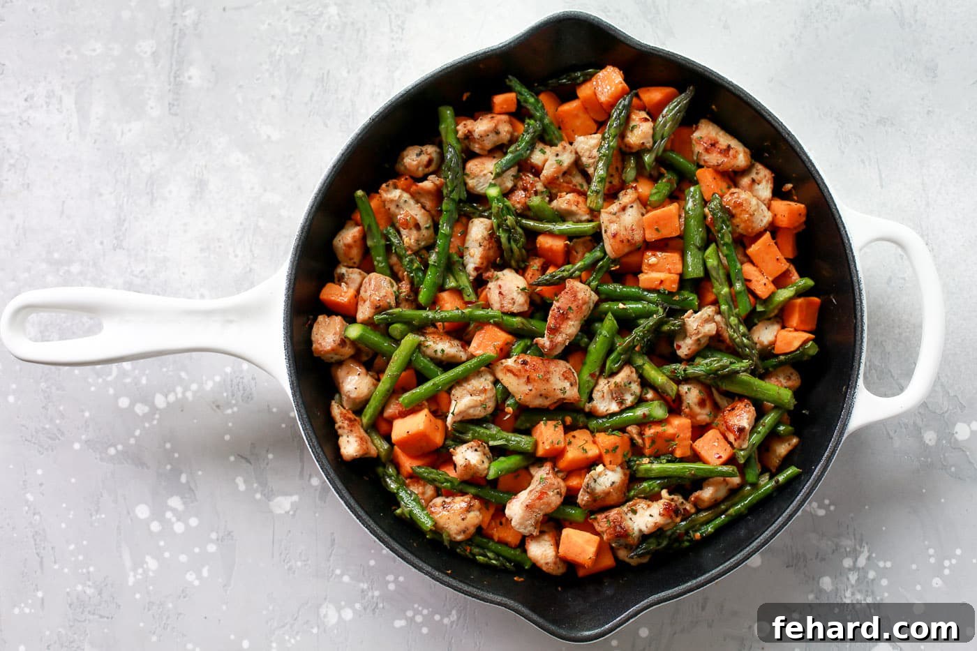 The one-pan meal taking shape, with chicken, sweet potatoes, and asparagus harmoniously cooking in the skillet.