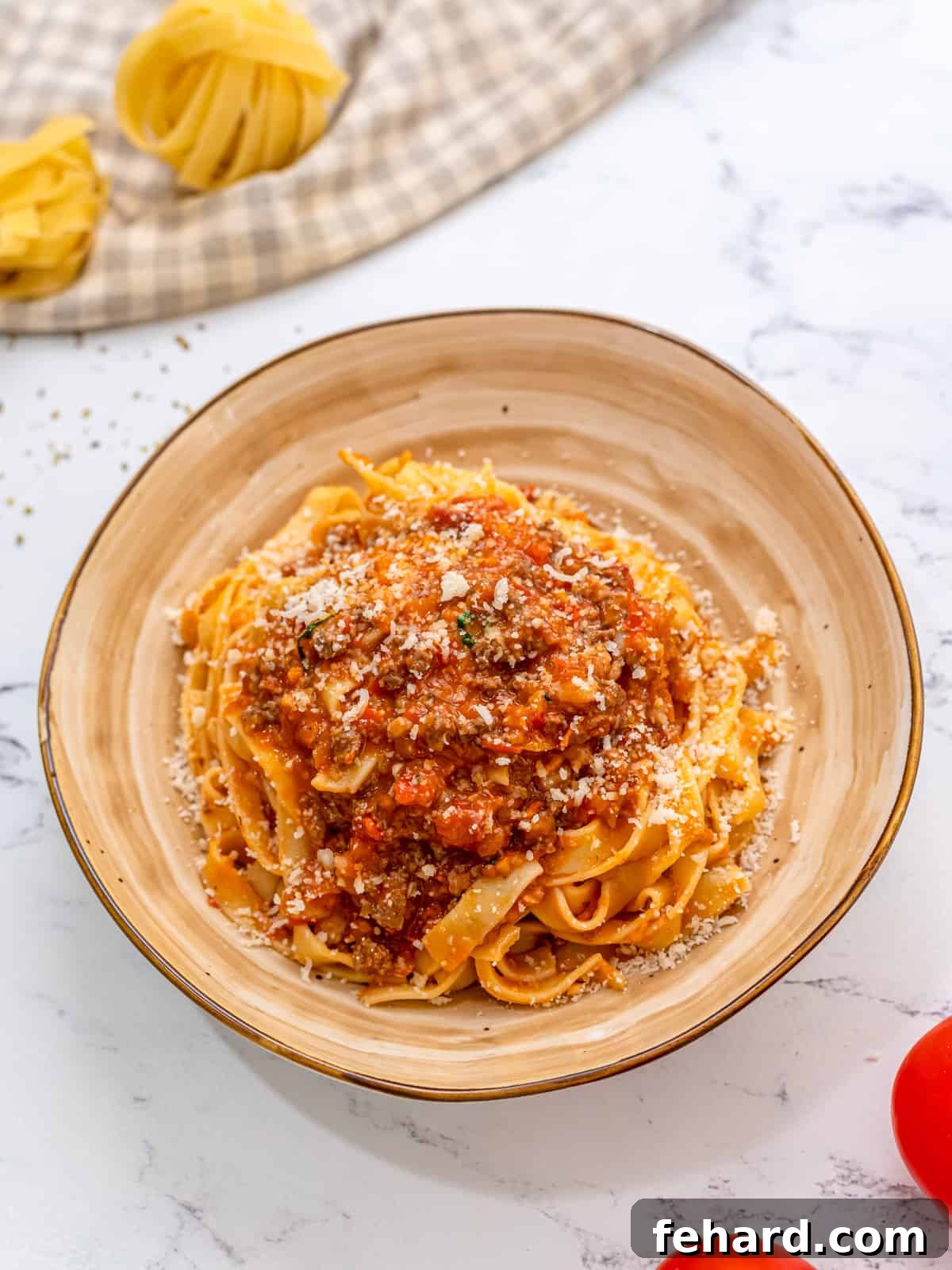 Hearty Bolognese Sauce served generously over tagliatelle pasta on a cream plate, garnished with fresh basil leaves and grated Parmesan cheese.