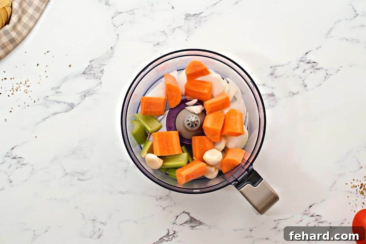 Finely minced carrots, onions, celery, and garlic in a food processor bowl, ready to be added to the Bolognese sauce.