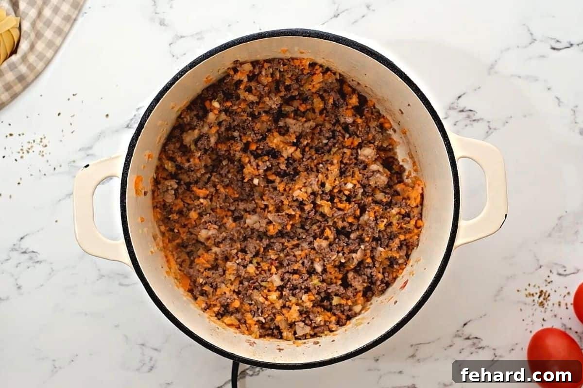 A mix of browned ground beef, Italian sausage, and softened soffritto vegetables simmering together in a large Dutch oven.