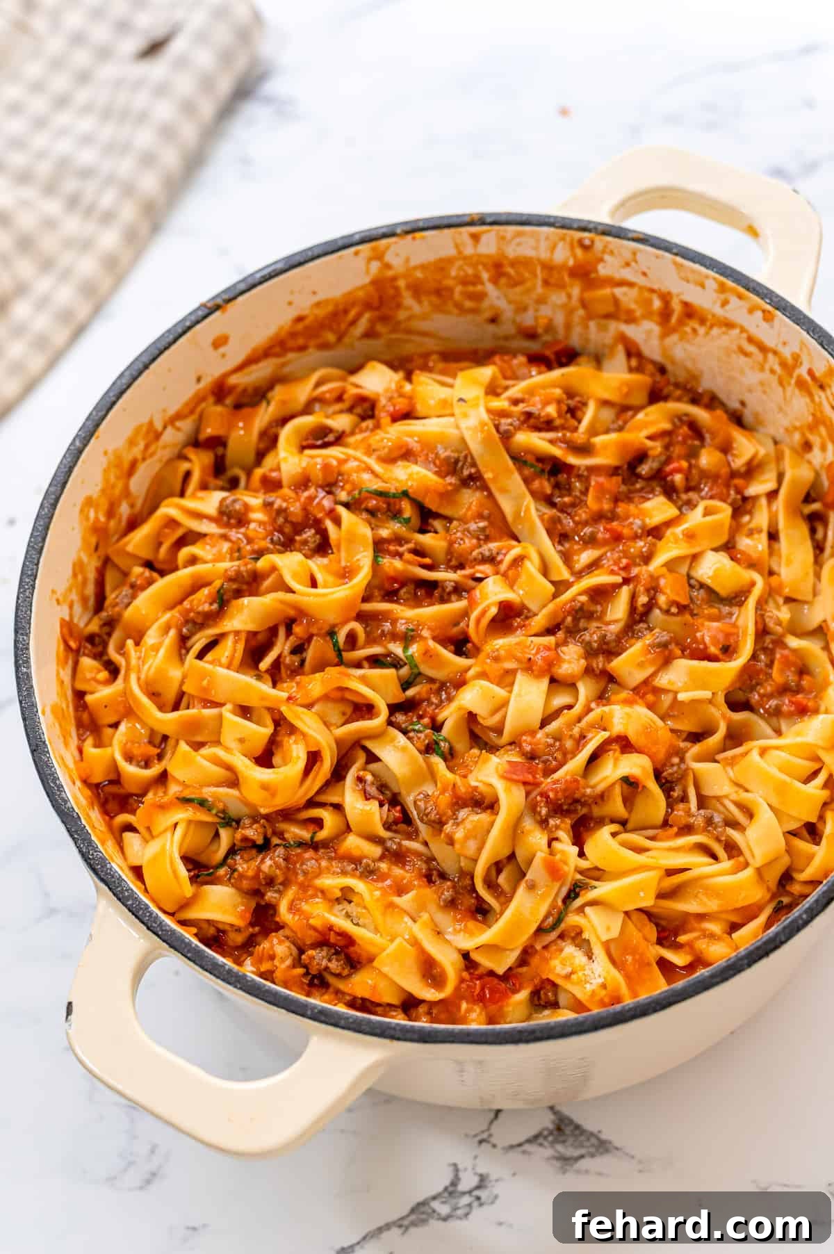 Freshly cooked tagliatelle pasta tossed with rich Bolognese sauce in a large Dutch oven, creating a hearty and inviting meal.