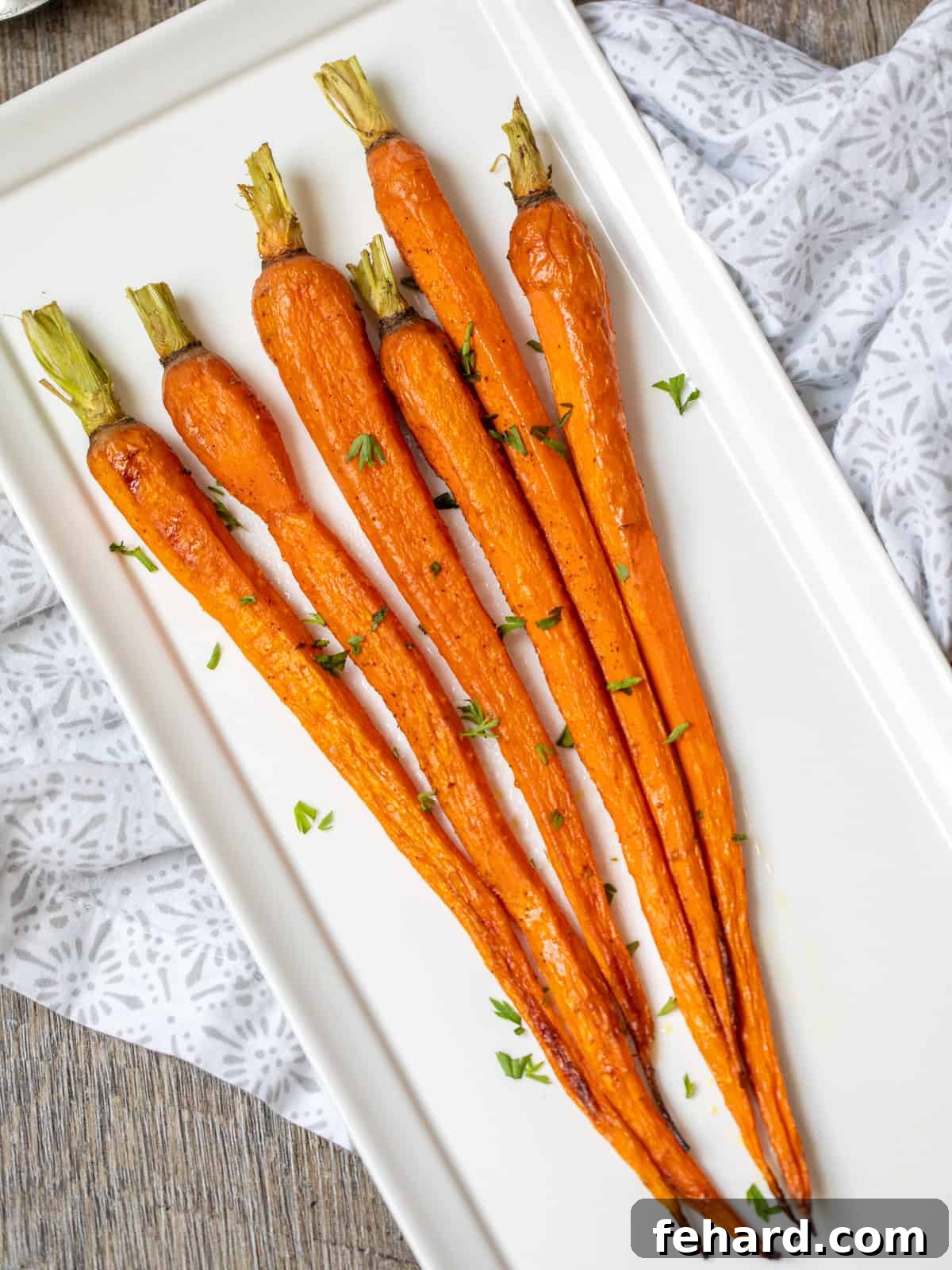 Golden Roasted Carrots 2 A white serving dish filled with large, golden-brown roasted carrots, highlighting their caramelized edges and tender appearance. Garnished with fresh herbs.