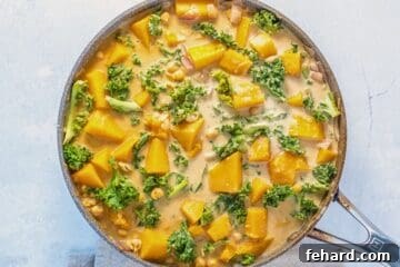 Butternut squash curry with kale and chickpeas, now incorporating creamy coconut milk, in a large skillet.