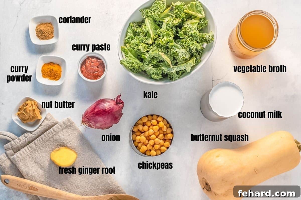 A selection of fresh ingredients laid out on a kitchen counter: butternut squash, kale, chickpeas, ginger, onion, and spices, ready for making curry.