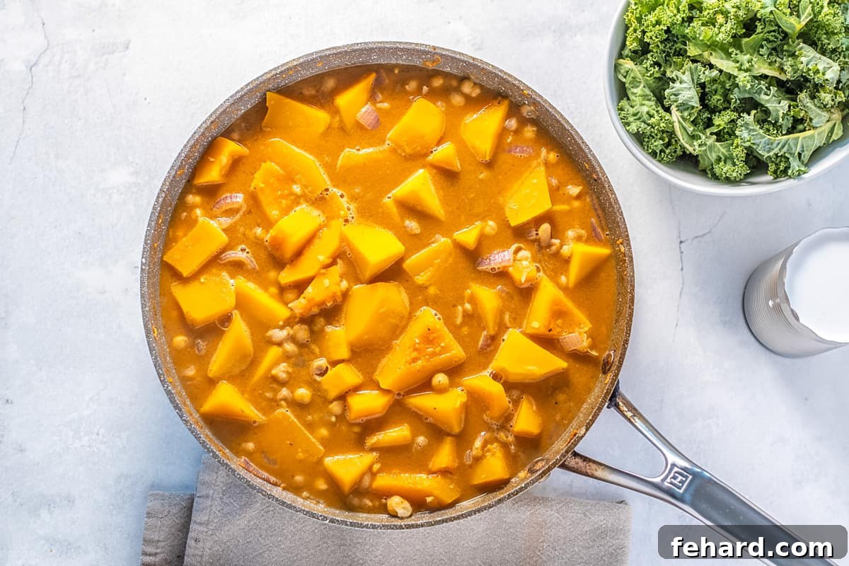 A saucepan filled with a vibrant orange curry base, tender butternut squash cubes, and hearty chickpeas simmering gently on the stovetop.