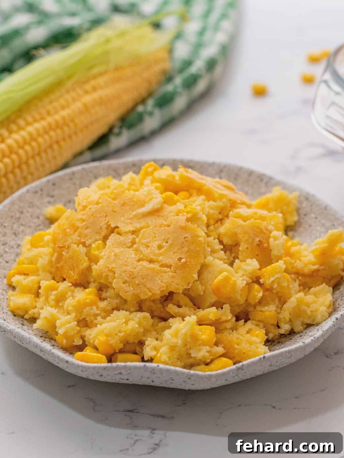 Plate with corn casserole. Next to fresh corn cobs.