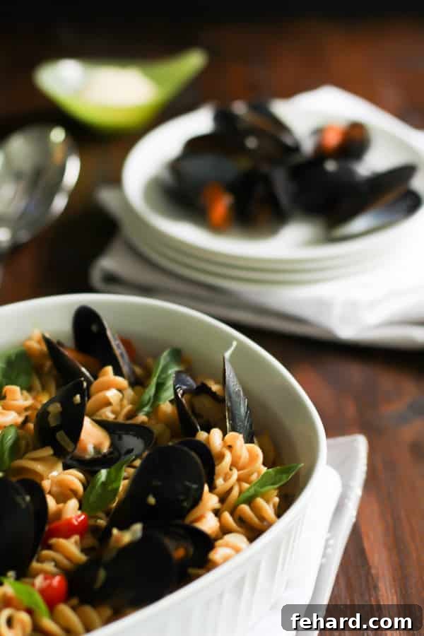 Whole Wheat Fusilli with Mussels Close-up view of Whole Wheat Fusilli with Mussels and cherry tomatoes, with a plate of cooked mussels in the blurred background.