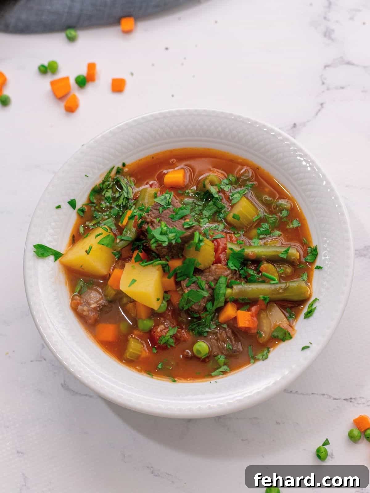 A steaming bowl of Old Fashioned Vegetable Beef Soup in a white ceramic bowl, garnished with fresh parsley.