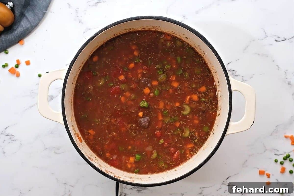 The rich braising liquid for Vegetable Beef Soup simmering in a large Dutch oven with red wine and diced tomatoes.
