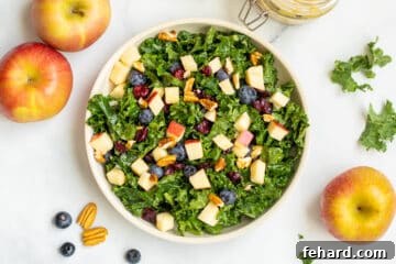 Kale salad with apples, berries and nuts in bowl with pecans and apples in background.