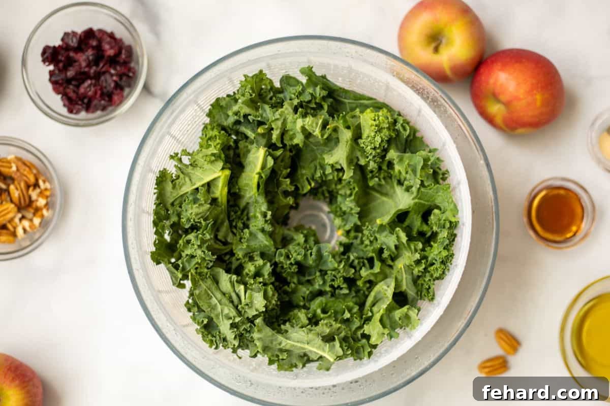 Freshly torn kale leaves drying in a salad spinner, positioned next to a small bowl containing the pre-mixed dressing ingredients.