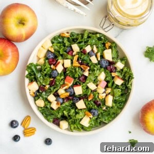 Kale salad with apples, berries and nuts in bowl with pecans and apples in background.