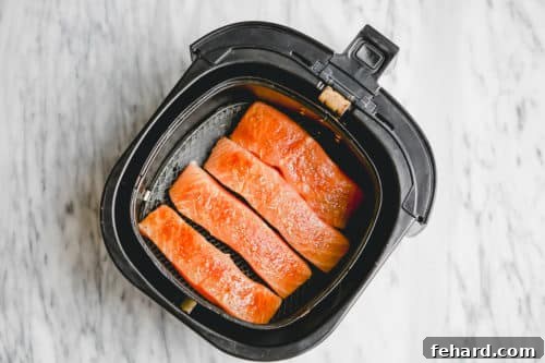 Overhead view of air fryer basket containing seasoned raw salmon fillets, ready to be cooked.