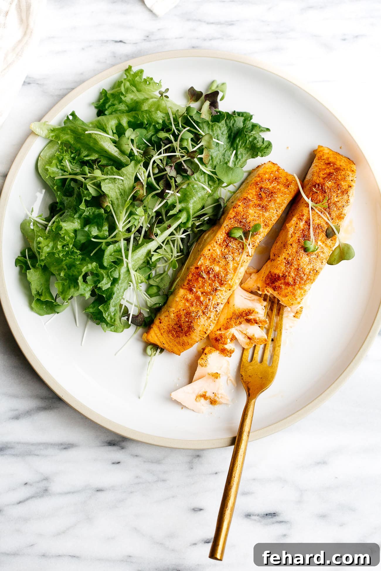 Overhead view of white plate containing air fryer salmon, garnished with lemon and herbs, ready to serve.