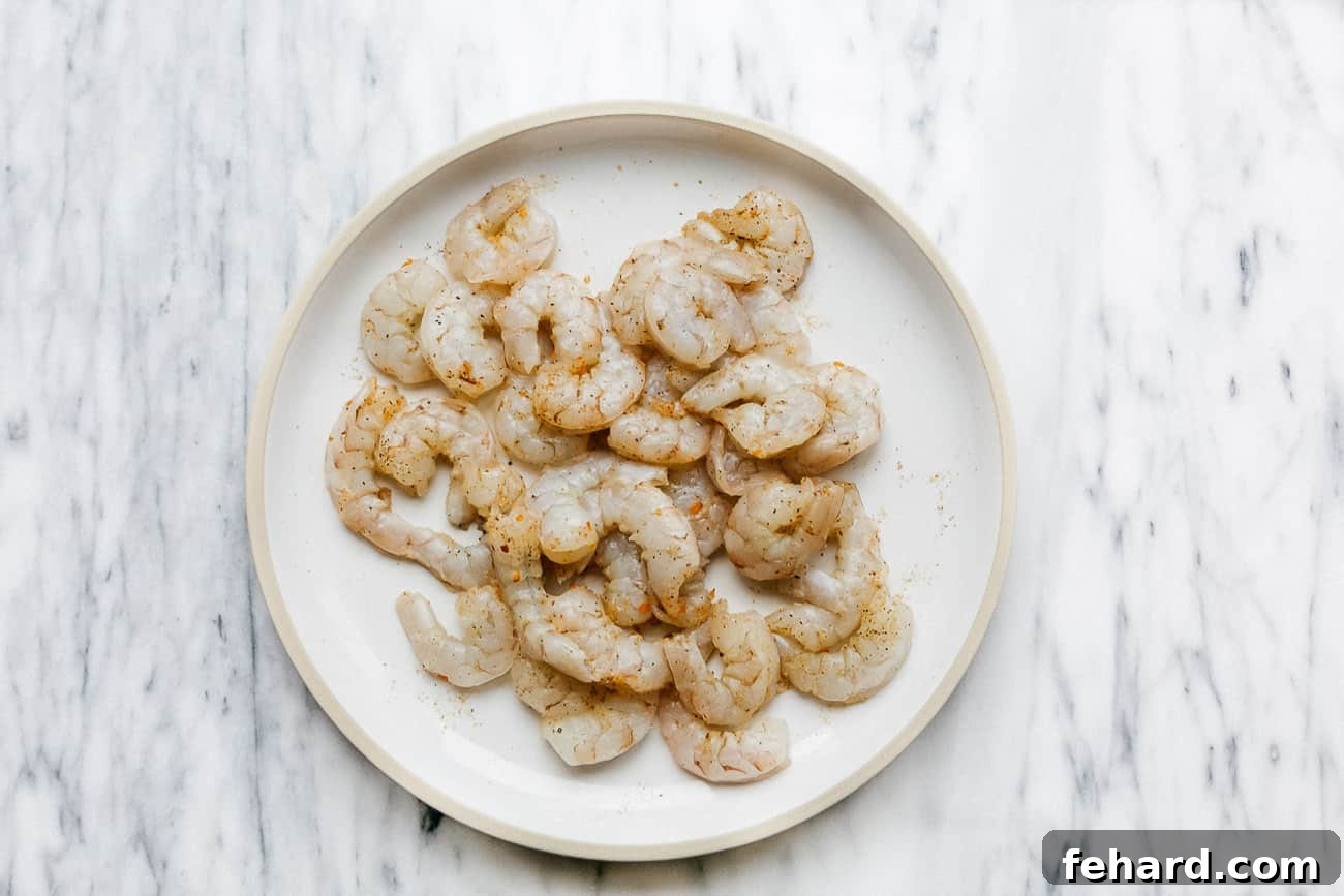 Crispy Air Fried Shrimp 3 Overhead view of raw shrimp being patted dry with paper towels on a white plate, emphasizing the importance of removing excess moisture.