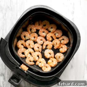 Close-up of an air fryer basket containing perfectly cooked, golden-pink shrimp.