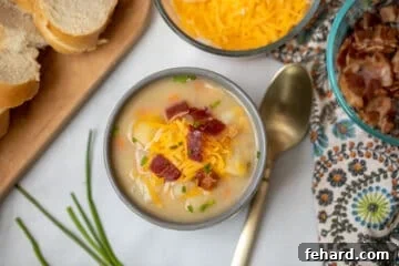 Bowl of potato soup topped with bacon, cheese, and chives, ready to eat.
