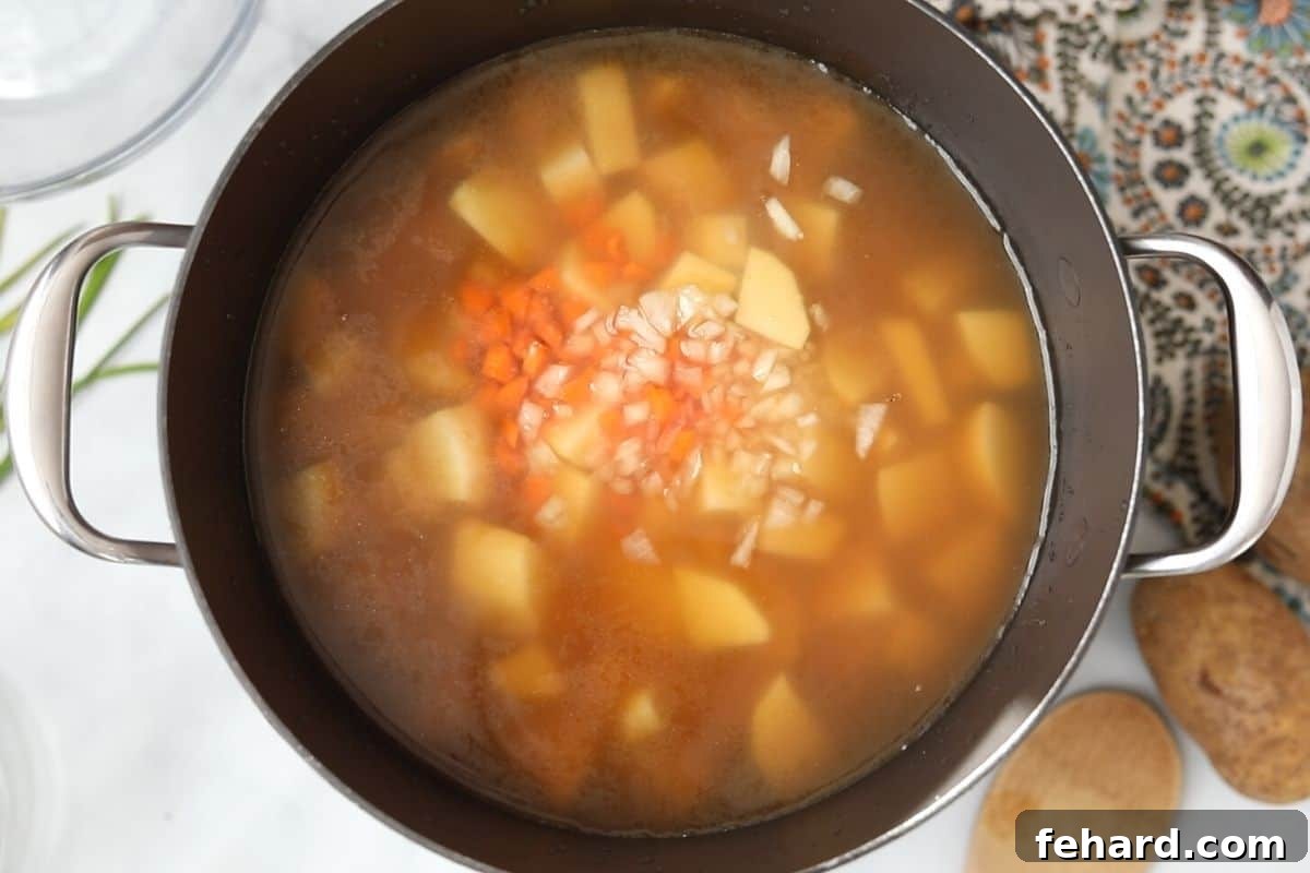 Potato Soup Recipe Steps Diced potatoes, carrots, and onions simmering in a stockpot with broth, creating the base for the potato soup.