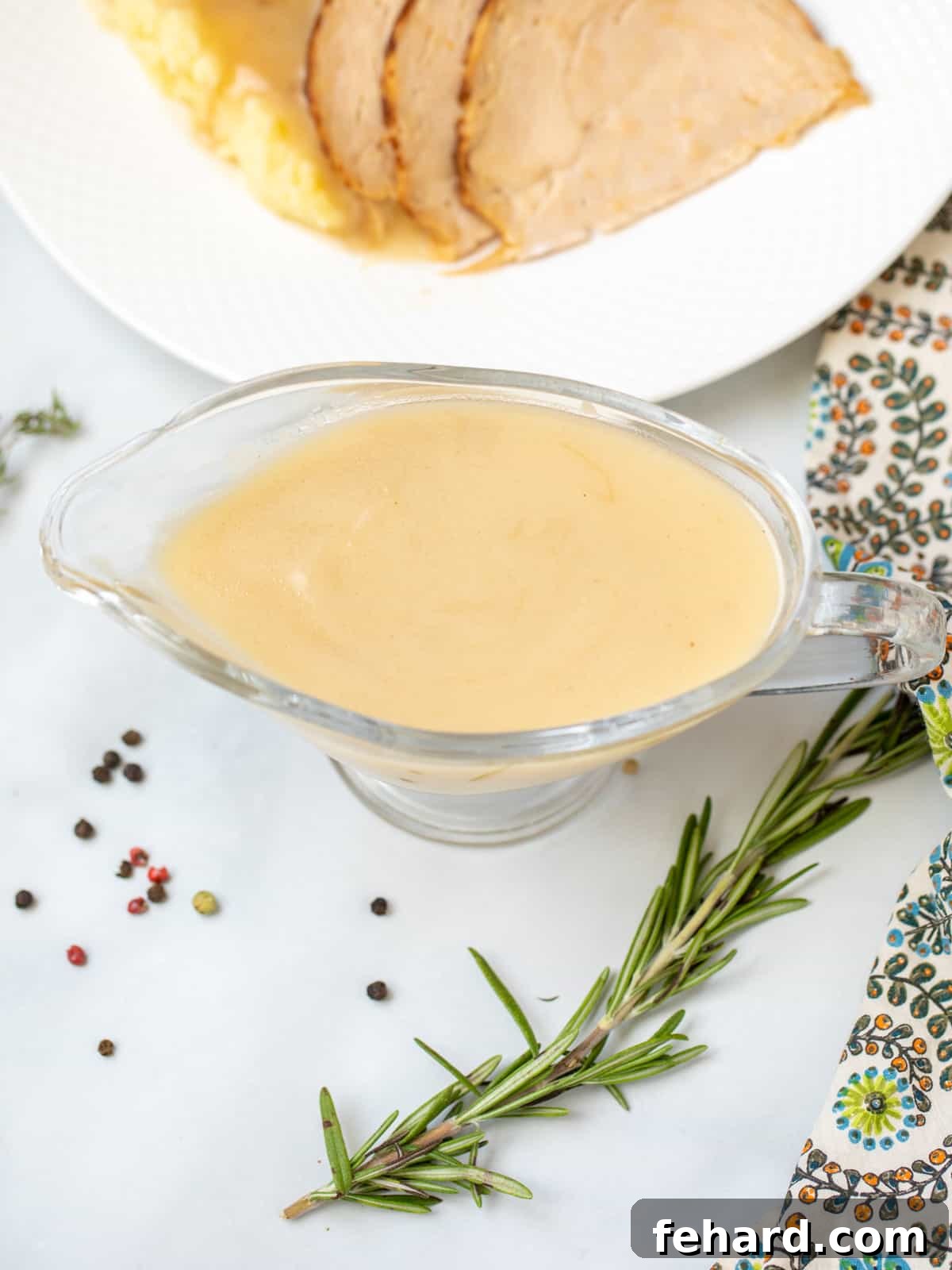 Perfect No-Drippings Turkey Gravy Recipe Clear gravy boat filled with smooth, golden turkey gravy next to perfectly sliced roasted turkey, ready to be served.