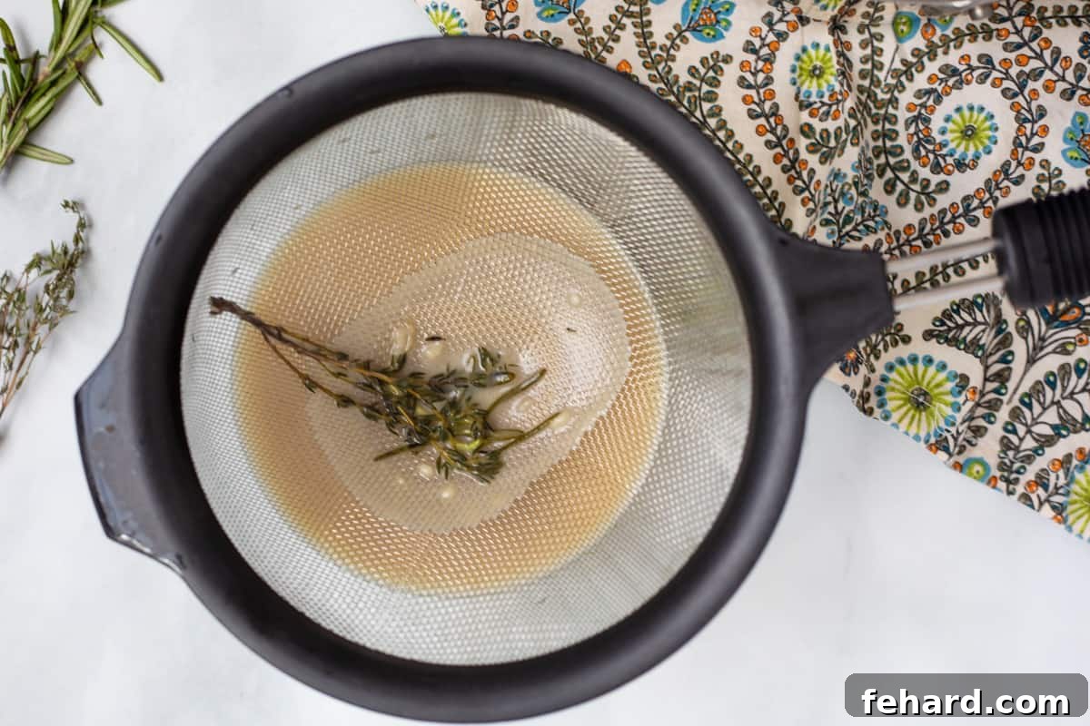 Stress-Free Turkey Gravy 5 Hot turkey gravy being strained through a fine mesh strainer into a bowl, removing impurities and herbs for a smooth finish.
