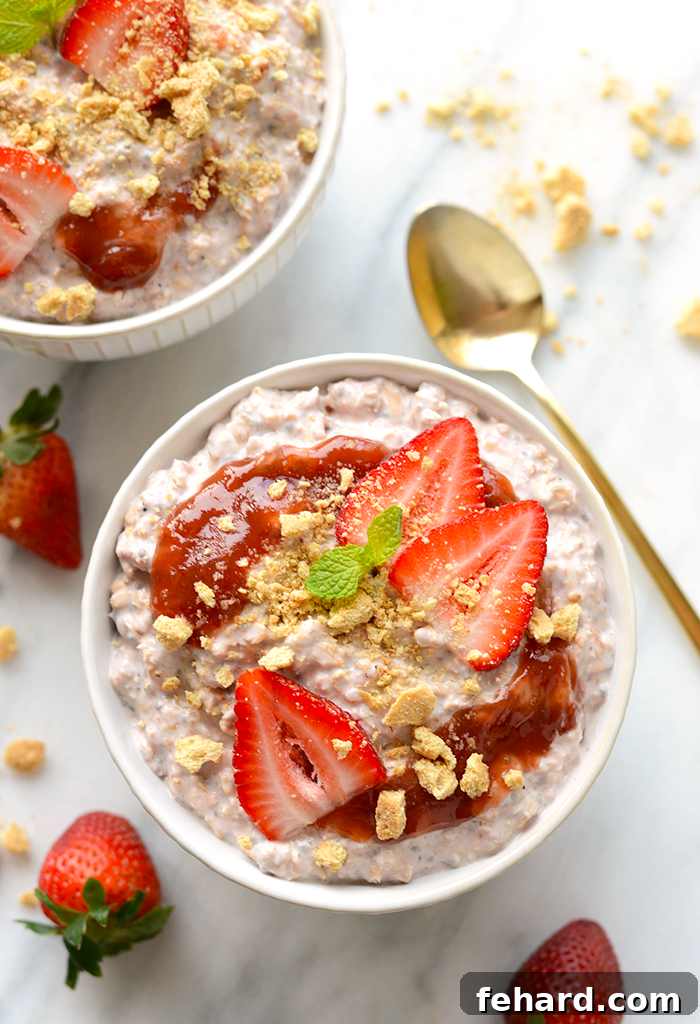A bowl overflowing with strawberry cheesecake overnight oats, beautifully garnished with strawberry jam, fresh sliced strawberries, and crushed graham crackers.