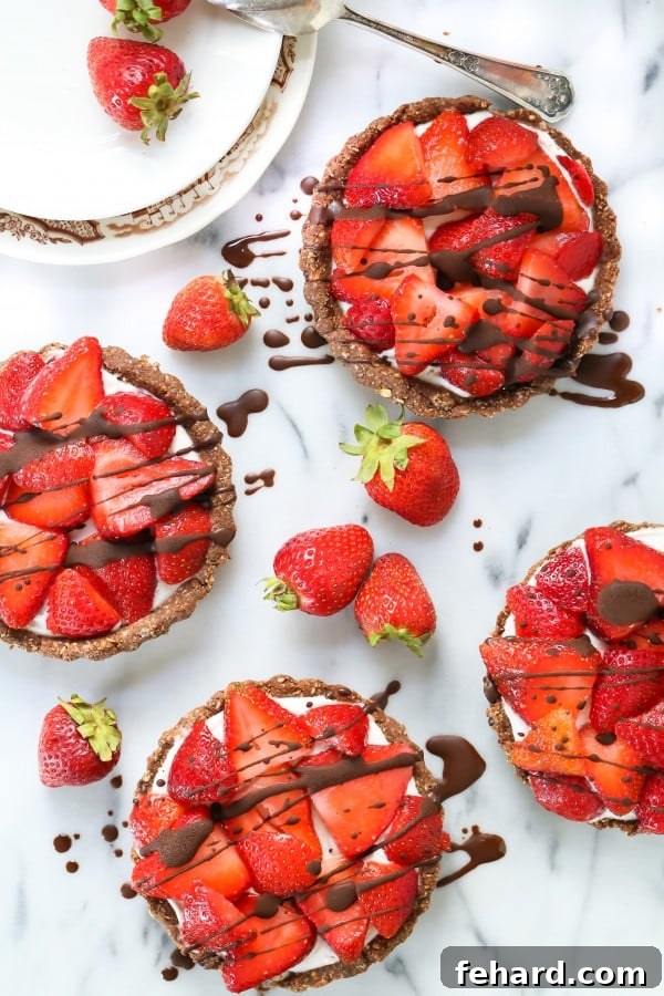 Four charming no-bake mini strawberry pies, elegantly drizzled with chocolate, presented on a plate.