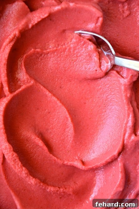 A close-up view of vibrant strawberry frozen yogurt, with a silver spoon gently resting inside, ready to be enjoyed.