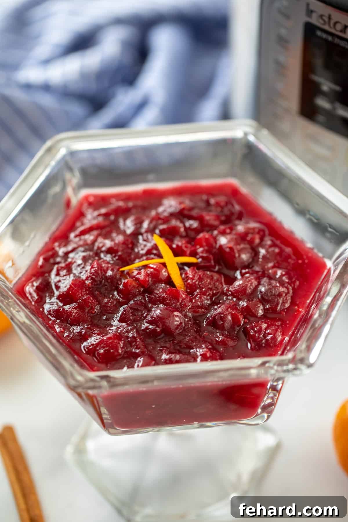 Instant Pot Cranberry Sauce Vibrant Instant Pot Cranberry Sauce in a clear glass serving dish, garnished with orange zest, positioned next to a modern Instant Pot.