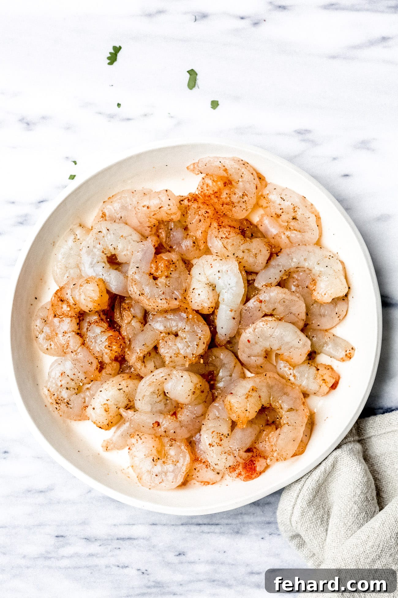 Raw shrimp meticulously seasoned with a vibrant blend of spices in a bowl, marinating and ready for grilling.