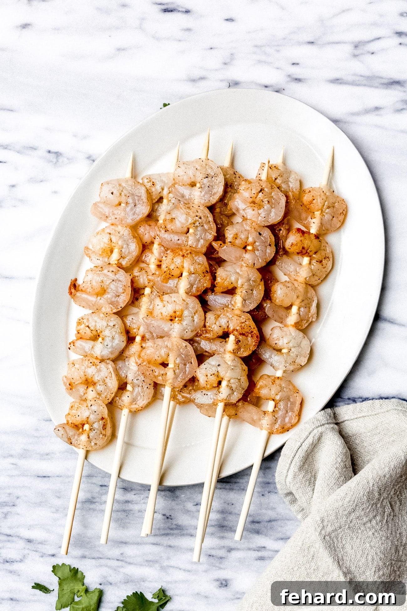 Perfectly threaded raw shrimp skewers neatly arranged on a pristine white plate, prepared for the grill.
