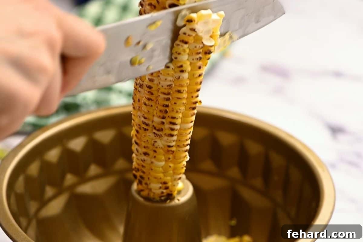 Grilled corn on the cob being sliced off into a Bundt pan, demonstrating a neat way to prepare the corn topping.