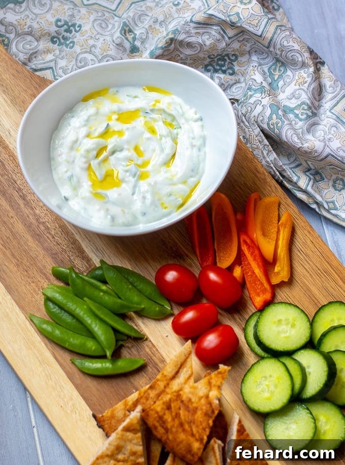 Homemade Tzatziki Sauce Bowl of Homemade Tzatziki Sauce in a white bowl on a cutting board, surrounded by fresh vegetables and pita bread, ready to be served.