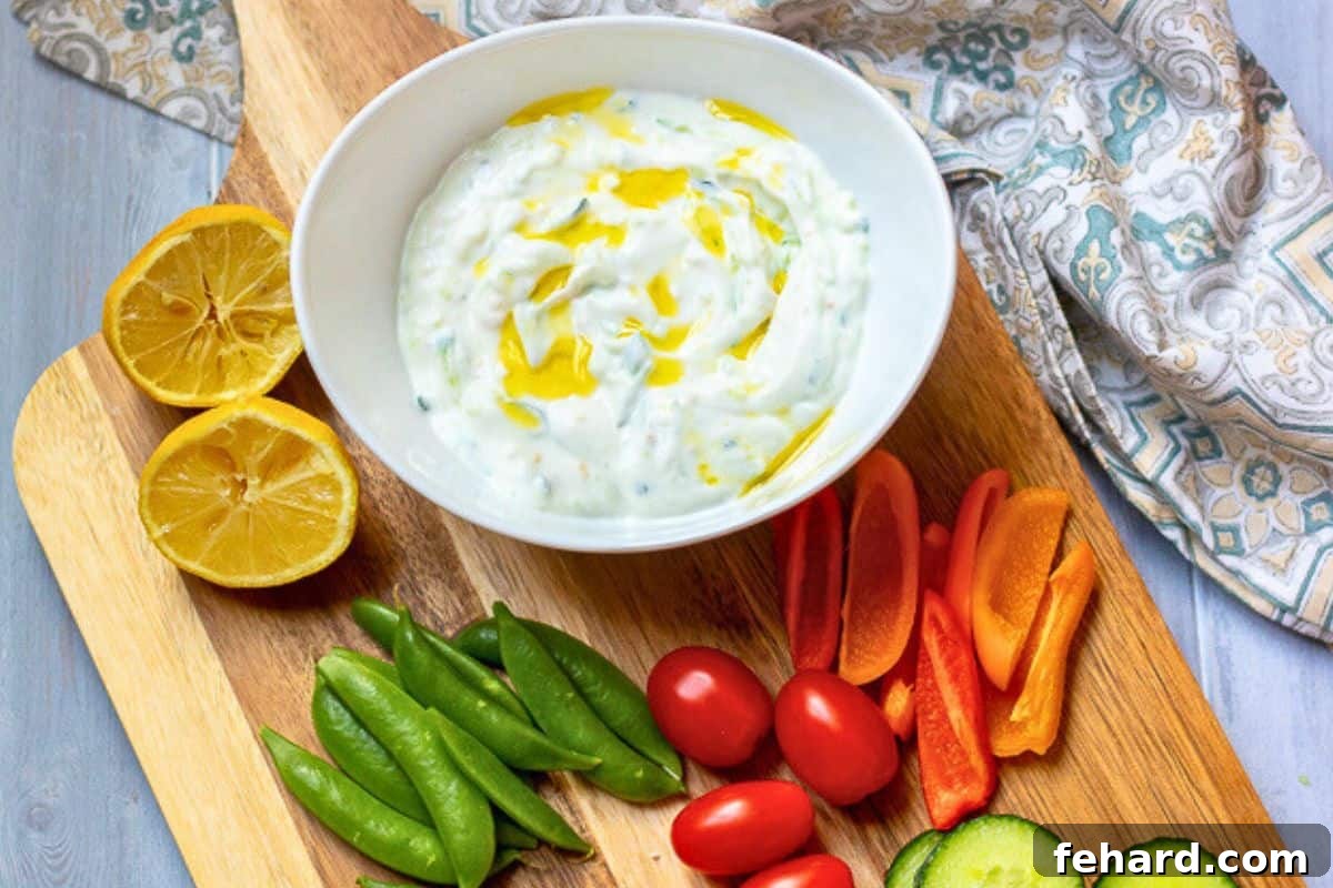 Easy Tzatziki Recipe Homemade Tzatziki sauce served in a small white bowl, garnished with a drizzle of olive oil, alongside a colorful assortment of fresh vegetables on a cutting board.