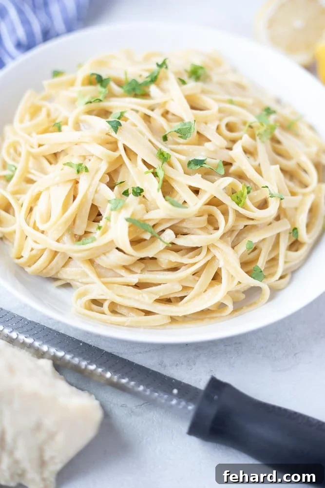 Bowl of low fat fettuccine alfredo next to Parmesan Cheese, showcasing a perfect 15-minute meal.