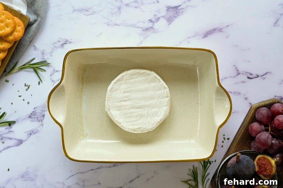 An unscored wheel of brie cheese placed in a small rectangular baking dish, awaiting baking, with fresh figs nearby.