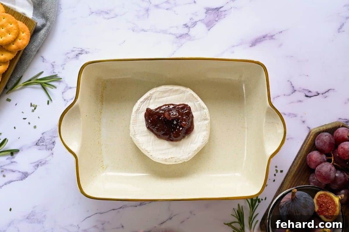 A wheel of brie cheese topped with fig jam, ready for baking.