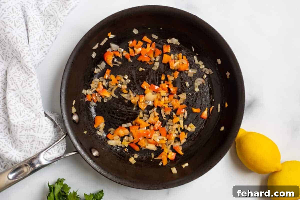 Minced shallots and finely chopped red bell peppers gently sautéing in a frying pan with olive oil, softening and releasing their aromatic flavors.